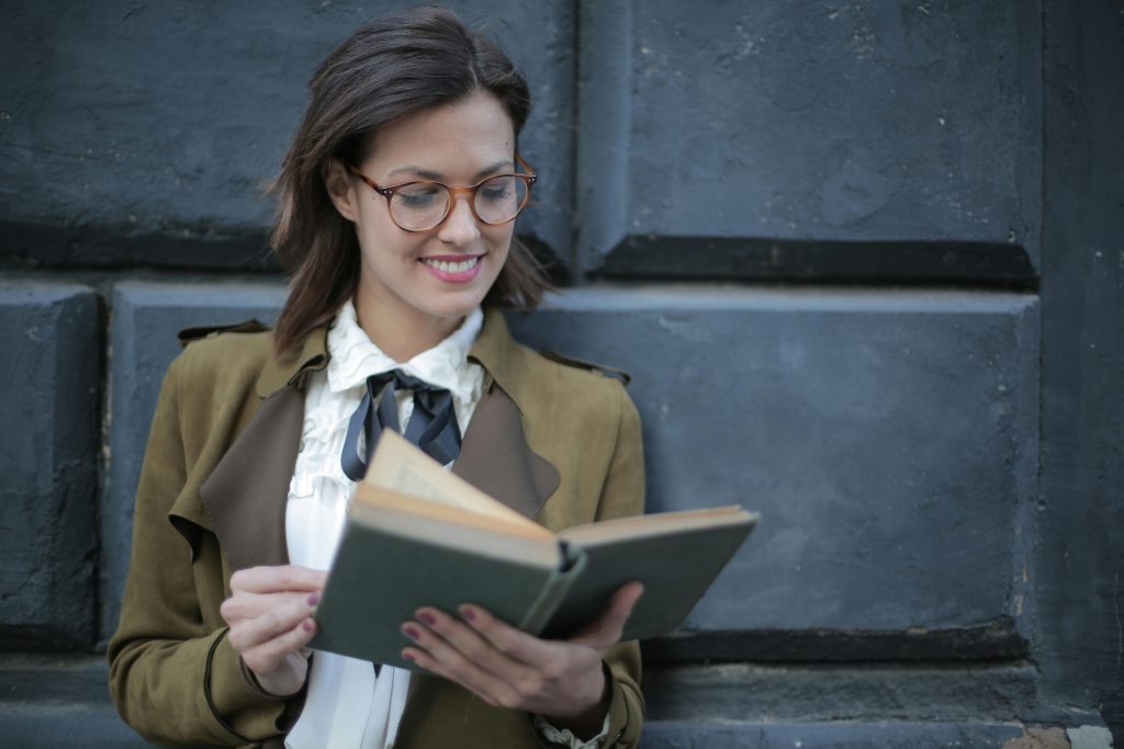 Happy adult woman reading book with interest on street