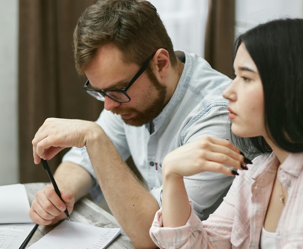 Man Wearing Eye Glasses Holding a Pen Sitting Beside a Woman